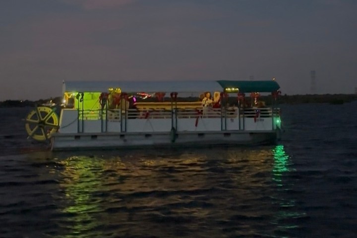 Boat with lights on water at dusk, paddle wheel visible on side.